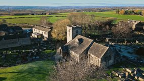 Panning aerial drone video footage of a small village of Hartshead with church and church yard, with gravestones and warm sunlight. Hartshead Moor, West Yorkshire, UK