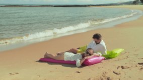 Young relaxed man in white shirt lying on inflatable mattress on sandy beach next to his peaceful wife sunbathing and enjoying rest during summer vacation at tropical resort - Powered by Shutterstock - Get 15% off with code: PIKWIZARD15
