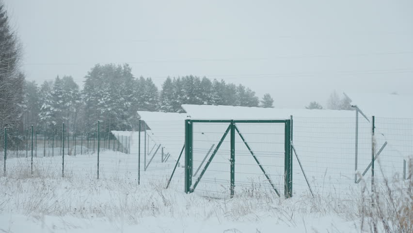 A black gate and fence on the solar park covered in thick snow during the winter in Estonia
