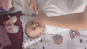 Vertical video. Young caucasian mother dressing her baby on changing table