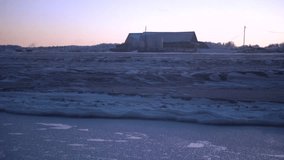 Landscape of frozen field with house on horizon in morning. Clip. Cold dark landscape of snowy field and old barn on horizon. Winter snow field in morning