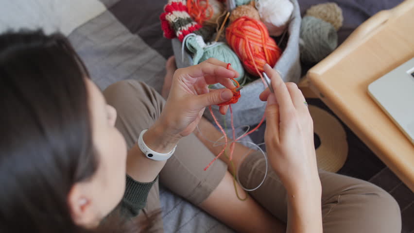Close-up video of woman knitting something small. Anti-stress hobby. Tranquil leisure at home. Handicraft. Online lessons for amateurs on laptop.