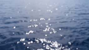 View of gentle waves from a boat moving through the Aegean Sea on a sunny day. The clip slowly moves into focus. Sunlight reflects off the water surface.