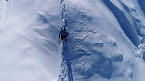 Стоковое видео: Top down view close up of adult man hiking on top of snowy mountain. Male mountaineer with trekking poles and a backpack walking on mountain ridge in Julian Alps
