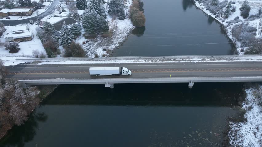 Semi truck driving across a bridge with snow covering the ground.
