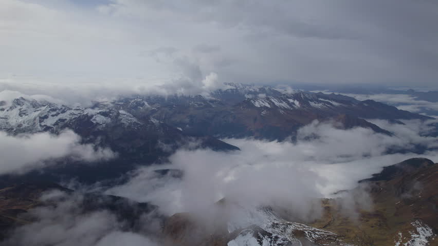 Aerial high angle shot above snowy mountains and clouds of Austria during daytime