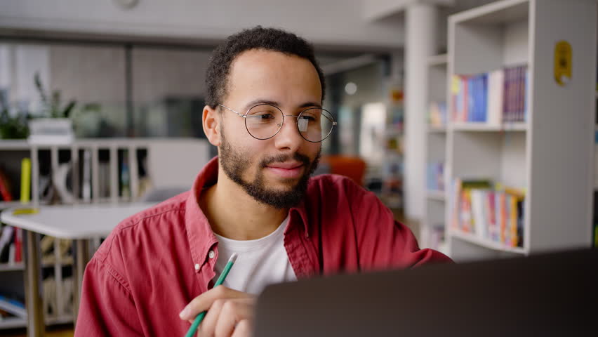 Close-up portrait of a confident determined cheerful African American university student, enthusiastically working on his diploma project or graduation work. Millennial successful university graduate Royalty-Free Stock Footage #1098332117