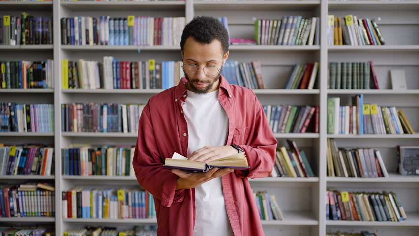 Waist length portrait African American student, university graduate, young tutor leafing through hardcover book encyclopedia while looking for informations for thesis, in the school library campus Royalty-Free Stock Footage #1098332215