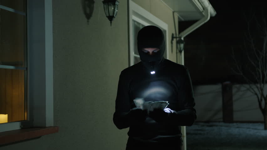 Unrecognized man in balaclava counting stolen money outdoors. Close-up shot of a burglar warned by the police before arrest. High quality 4k footage