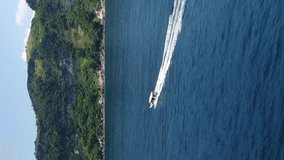 Vertical video of Aerial shot of boat going along steep cliffs