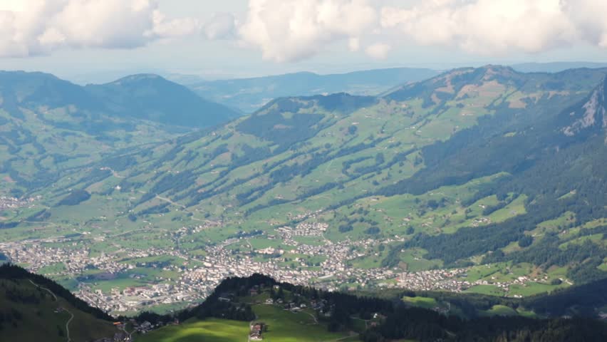 Beautiful mesmerizing view of a mountain landscape with a settlement and white clouds in the sky in fronalpstock switzerland, close-up side view in slow motion and tracking to the left.