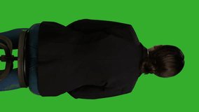 Vertical video: Back view close up of female manager waiting on chair before corporate meeting, sitting in studio with greenscreen background. Woman dressed in office suit working as employee or