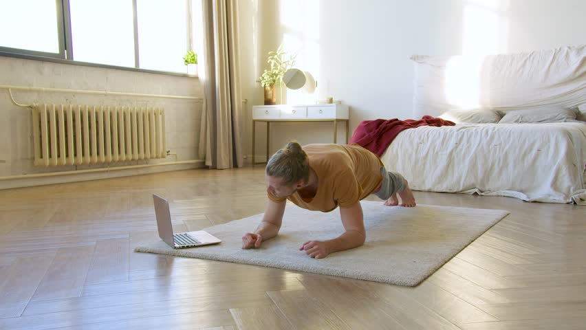 Young man in front of laptop monitor doing the plank exercise. Home workout. He follows the guidance of his online coach. Healthy lifestyle concept. | Shutterstock HD Video #1098341151
