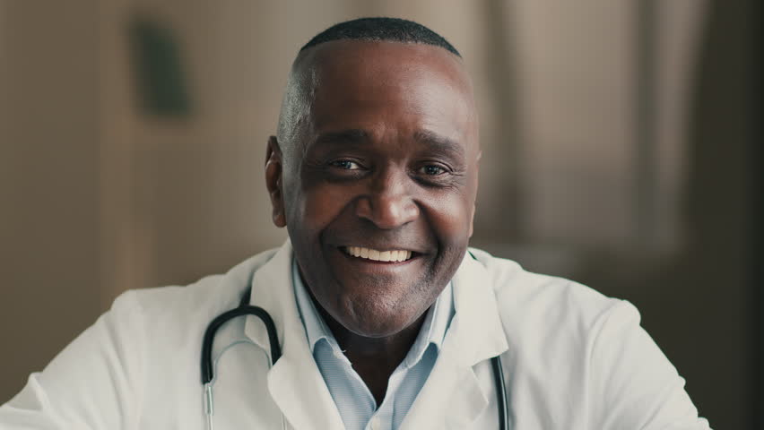 Senior male doctor african man medical practitioner makes distant video call middle-aged adult physician talks to camera consulting patient online in web chat records healthcare webinar webcam view | Shutterstock HD Video #1098343415
