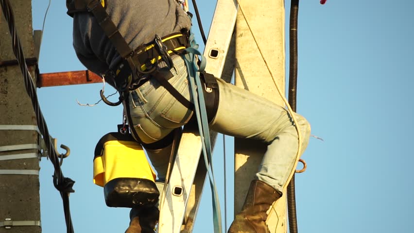 Skilled electrician in helmet fixes wires standing on ladder near high pole against blue sky on summer day backside view. Electrical service and mounting on the pole. Slow motion Royalty-Free Stock Footage #1098346531