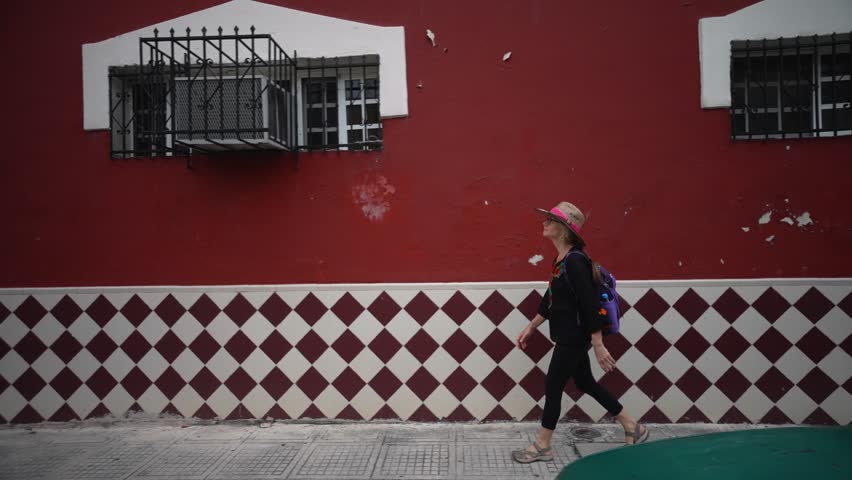 Pretty, mature, woman walking on a sidewalk along colorful buildings in Merida, Yucatan, Mexico.
