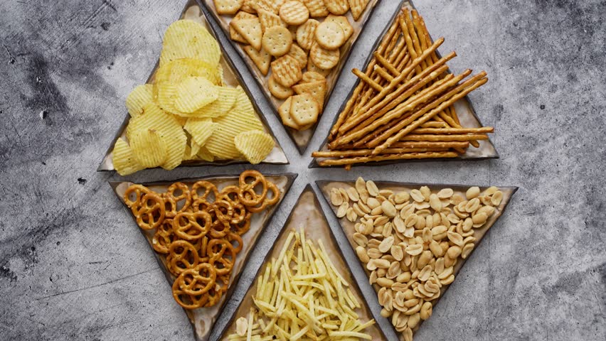 Mix of snacks served on small triangle plates. Pretzels, crackers, chips, nuts, sticks