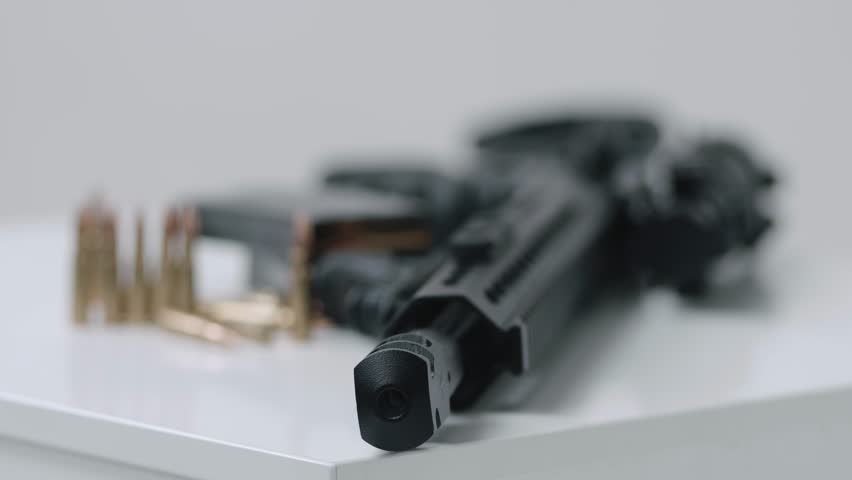 High angle dolly in towards loaded assault rifle with a small amount of ammunition in the foreground. military target, war, bullet weapon, army military firearm, bunch of bullets, bullet shells