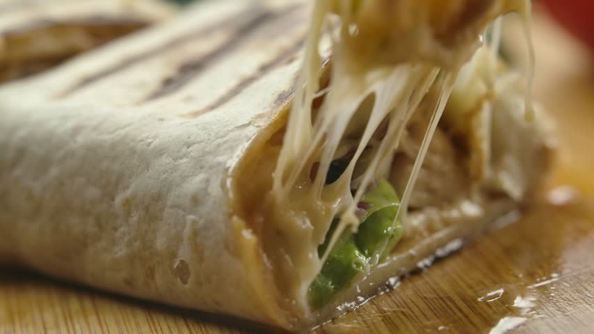 Super close-up of mexican burrito with melted cheese and Juicy pieces of meat and vegetables fall out of the burrito. High quality 4k footage | Shutterstock HD Video #1098354995