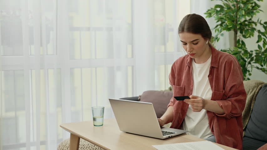 Caucasian young woman sitting at home, using laptop and credit card for online shopping, entering data for payment, online transaction or order home delivery. Banking operations | Shutterstock HD Video #1098355213