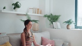 Video of confident woman in lotus position sitting on the sofa at living room at home.