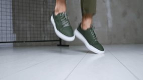 Man in khaki jeans and sneakers jumps demonstrating comfortable sport shoes. Close up. Fashionable stylish footwear presentation in studio.