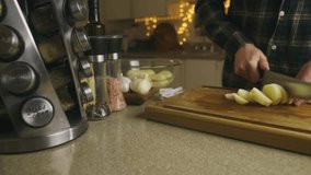 Video. A man in the home kitchen prepares lunch from healthy organic products. Cutting potatoes on a cutting board. Lots of ingredients on the kitchen table, kitchen appliances. Home interior.