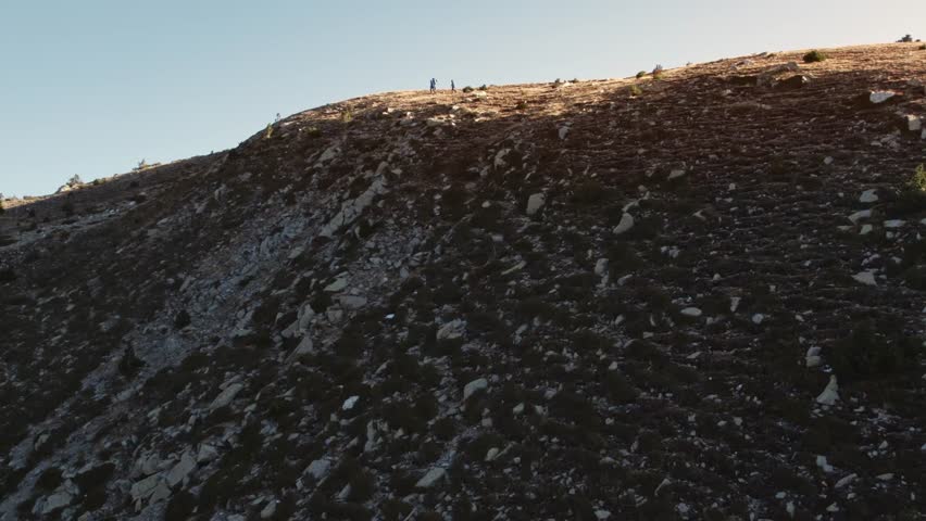 Aerial, group of three healthy fit people hiking on a exposed hill ridge