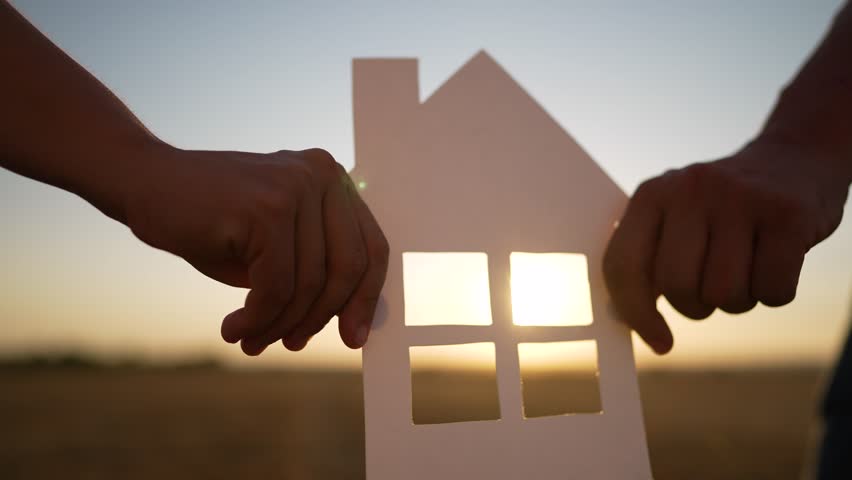 Happy family. People hands hold a paper house together. House made of paper is symbol of family happiness, mortgage protection, ecology. Sun shines through the window of house in nature at sunset | Shutterstock HD Video #1098372127