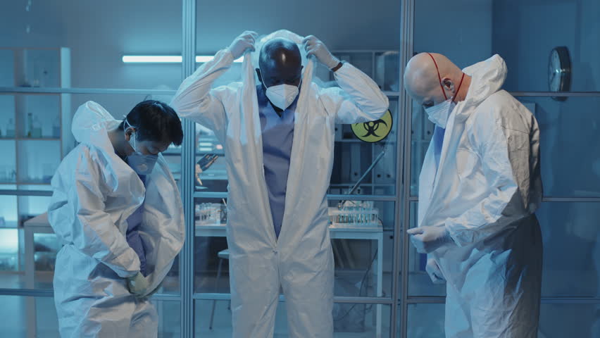 Medium long of three diverse doctors putting on white hazmat suits in laboratory | Shutterstock HD Video #1098373193