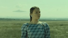 Portrait of woman walking on field . Surreal extraterrestrial footage . UFO flies over the field . Flying saucer fly over in the sky . Surrealistic scene . Shot on ARRI ALEXA cinema camera slow motion