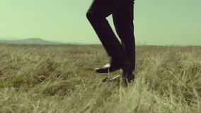 Close up side view of men's legs walking or standing on field . Young stylish lonely man on meadow field at day time . Shot on ARRI Alexa Camera in slow motion