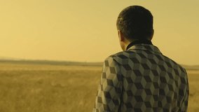 Rear , back view of lonely man walking or standing on field . Young stylishman on meadow field at evening time . Shot on ARRI Alexa Camera in slow motion