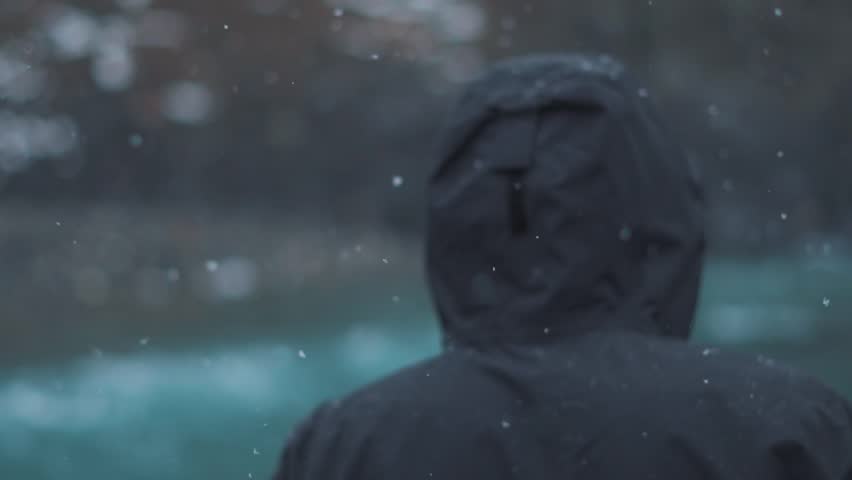 Rear view shot of an Indian man wearing jacket walking in front of the flowing river during the snowfall at Sissu in Lahaul Spiti district of Himachal Pradesh, India. Man walking in the snowfall. 