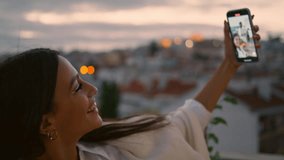 Positive woman taking selfie in sunset balcony closeup. Happy lady making smartphone photo with husband. Cheerful people having fun in luxury hotel evening date. Positive girl videocalling cellphone  - Powered by Shutterstock - Get 15% off with code: PIKWIZARD15