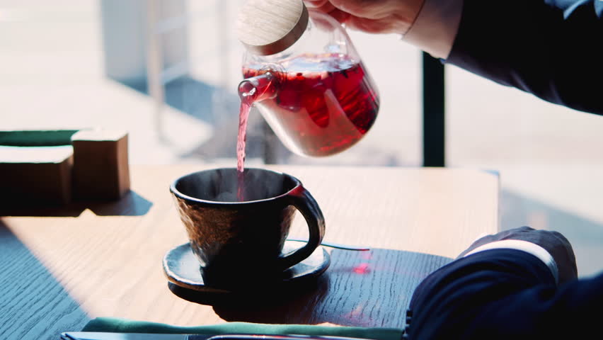 Close-up shot of cafe visitor pouring tea from teapot to beautiful original clay teacup. Aromatic hot beverage with fruits filling air with aroma. Interesting conceptual dishes in restaurant. | Shutterstock HD Video #1098378129