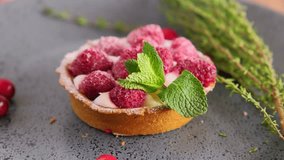 Raspberry tartlet with custard cream decorated with mint leaf and fresh berries slowly rotating on a plate, mini tart cake, close up video of sweet dessert, slow motion video clip, 4k footage