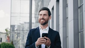 Smiling man walking on street near office building holding phone happy businessman browsing internet news using smartphone checking email writing text message in social network uses mobile application - Powered by Shutterstock - Get 15% off with code: PIKWIZARD15