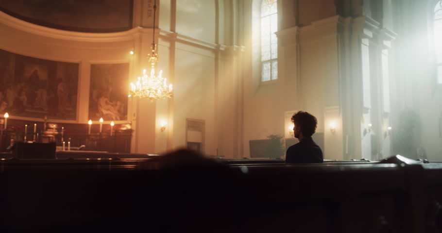 Young Christian Man Sits Piously in Majestic Church, with Folded Hands He Seeks Guidance From Their Religious Faith and Spirituality while Praying. Christianity and Belief in Power and Love of God Royalty-Free Stock Footage #1098380835