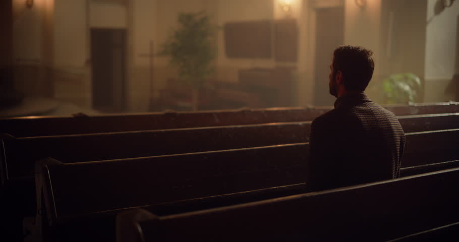 Christian Man Sits Alone in Church, Praying, Seeks Guidance from Religious Faith and Spiritual Belief in the Lord. Cinematic Camera Capturing the Spirit of Christianity and Forgiveness of God Royalty-Free Stock Footage #1098381029