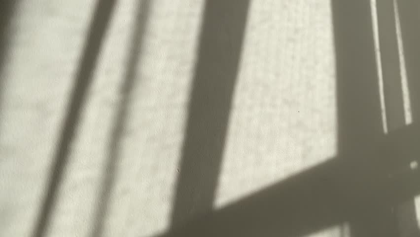 The shadow of the translucent curtain of the window on the wall gently moved by the wind. The sun shines in the afternoon.