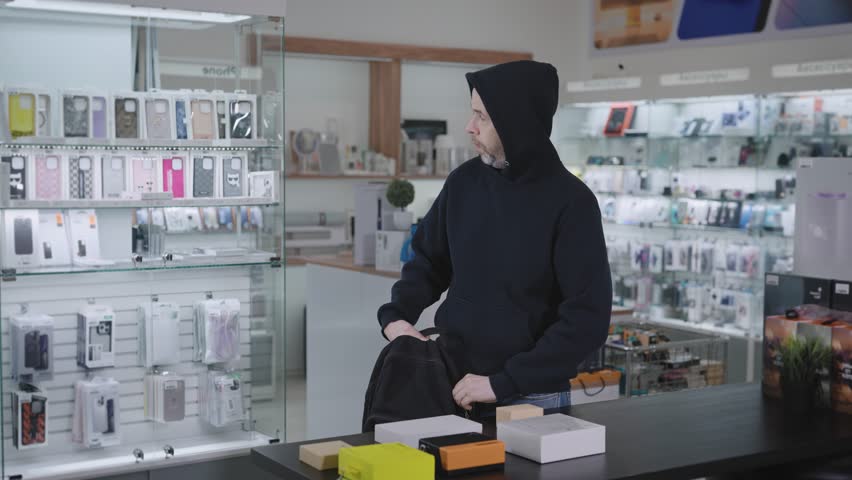 Suspicious man steals in a gadget store. The thief hides the goods and runs away from the store. Royalty-Free Stock Footage #1098383957
