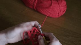A girl crochets using a red thread. Handmade. Home hobby. 4k video.