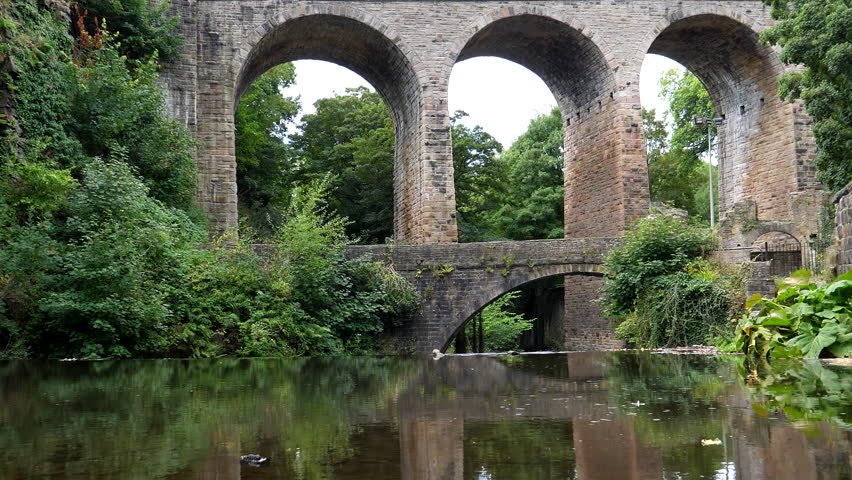 Tall old stone arch Union Road Bridge in New Mills Peak District National Park on river Goyt in summer, low angle viewpoint before weir.