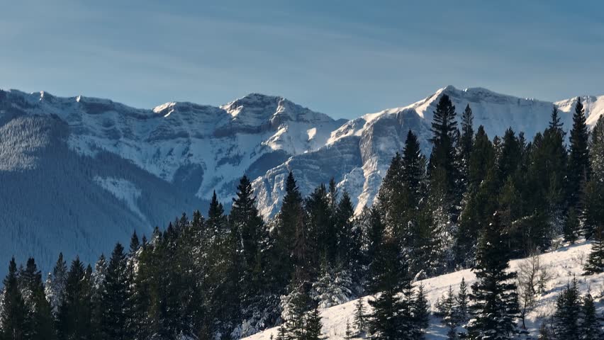 Parallax shot of mountain tops moving behind evergreen trees on a ridgeline in the foreground in the Canadian Rocky Mountains Royalty-Free Stock Footage #1098388891