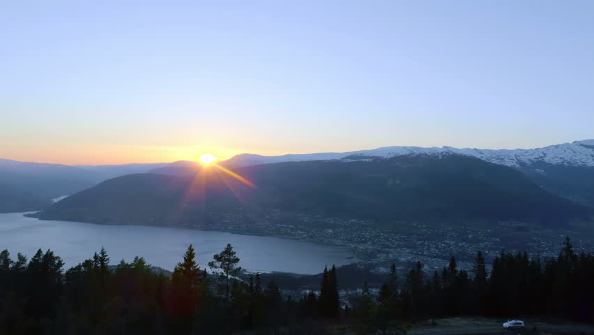 High angle shot over town houses at foothills of mountain range beside river flowing at sunset during evening time.