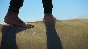 slow motion man walking barefoot on sand. camera follows male feet. coastal dunes. desert environment, lack of moisture hinders the growth of vegetation 