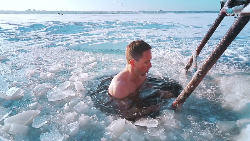 Winter swim. Young man swims in the ice hole