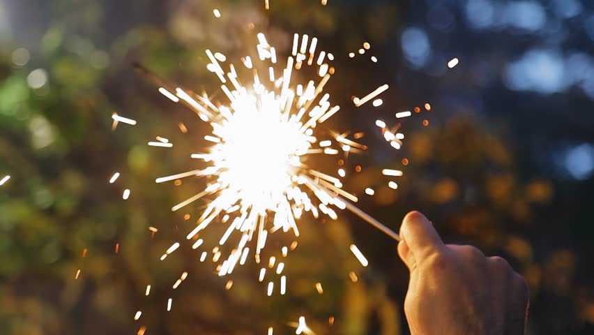 A man holds a burning sparkler in his hands. Sparks from the fire fly in different directions | Shutterstock HD Video #1098402205
