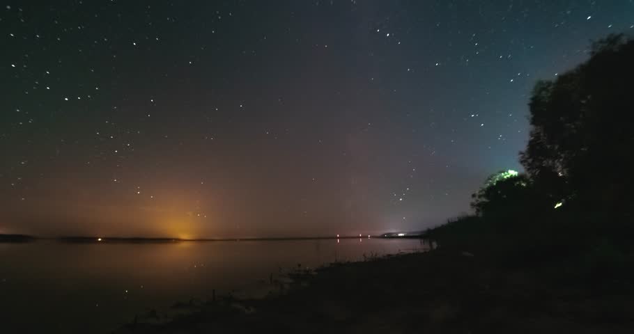 Timelapse of night sky with stars above flat calm lake. Milky way is visible